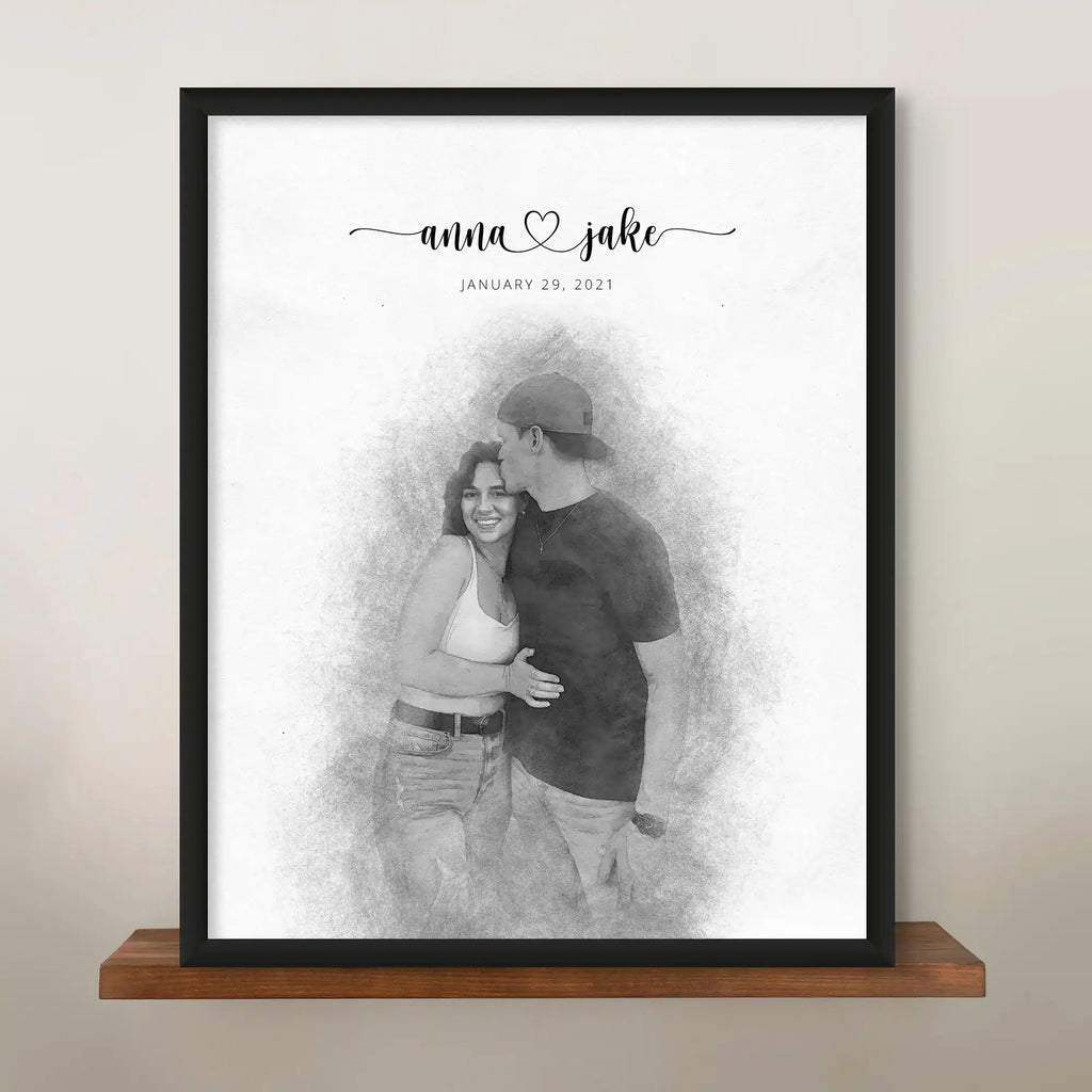 Sketch-style portrait of a couple, the man kissing the woman's forehead, in a black frame on a wooden shelf