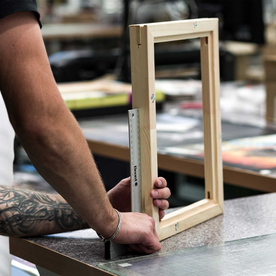 A framer checks the corner of a wooden picture frame with a square on the workshop bench