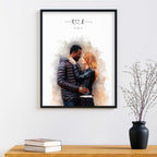 Watercolor-style portrait of a couple embracing, in a black frame above a wood table with books and a vase of twigs